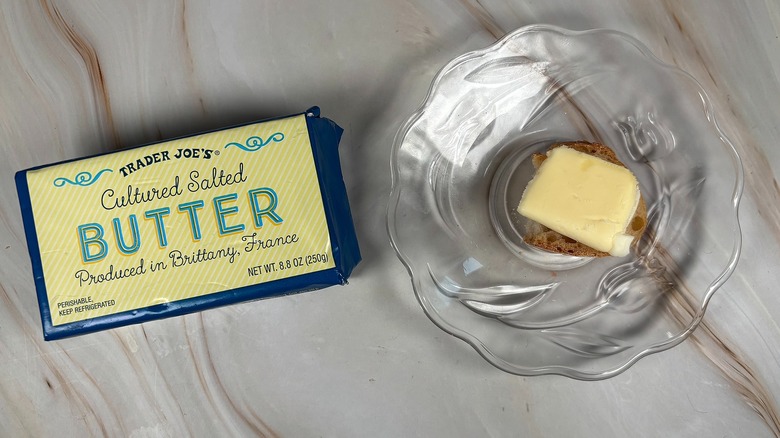 Package of Trader Joe's salted butter next to glass plate with piece of baguette and butter