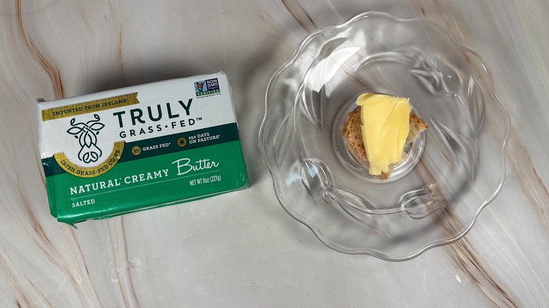 Package of Truly salted butter next to glass plate with piece of baguette and butter