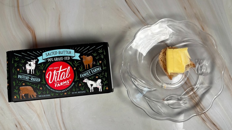 Package of Vital Farms salted butter next to glass plate with piece of baguette and butter