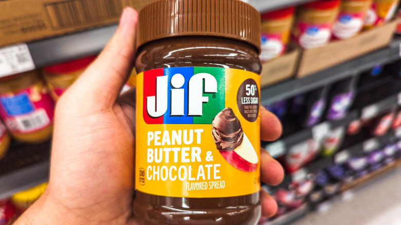 Hand holding Jif peanut butter and chocolate spread in grocery store aisle
