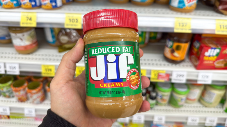 Hand holding plastic container of Jif reduced fat peanut butter in grocery store aisle