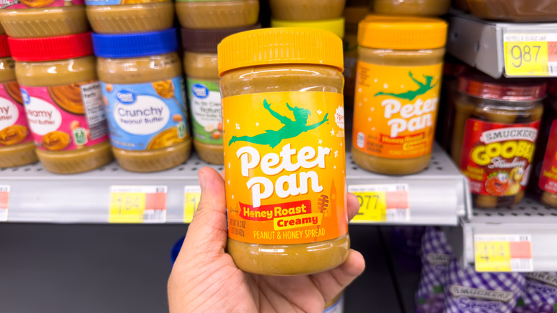 Hand holding Peter Pan creamy honey roast peanut butter in grocery store aisle