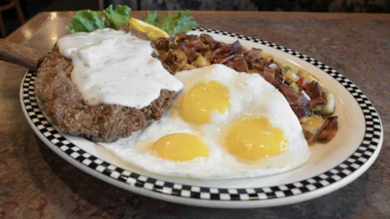 A chicken fried steak served with three eggs and potatoes