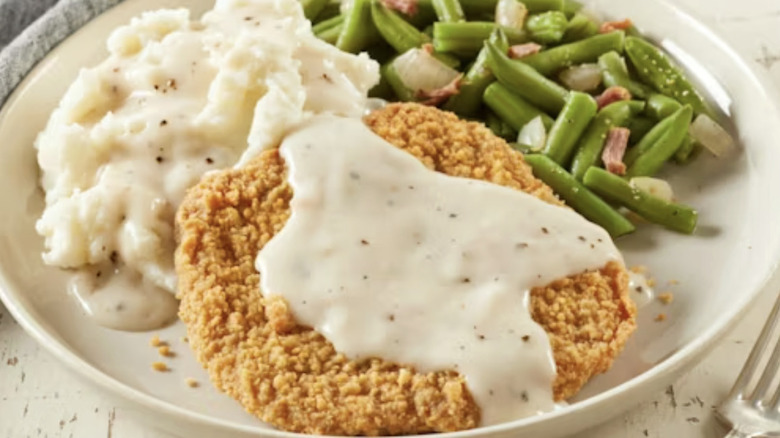 A chicken fried steak served on a white plate with green beans and mashed potatoes