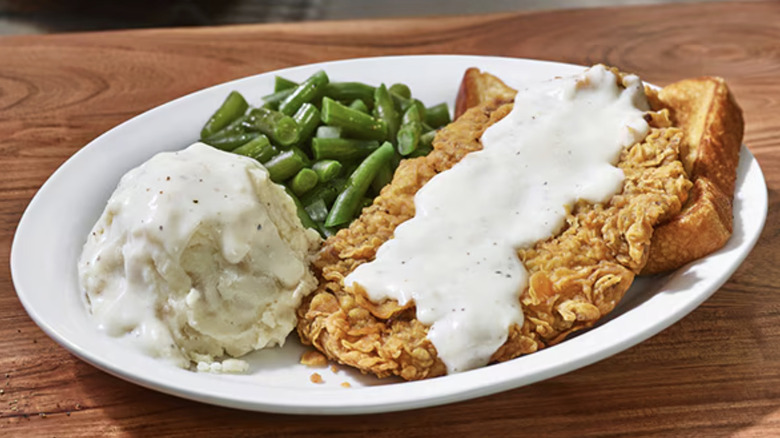 A chicken fried steak served with green beans, toast, and mashed potatoes