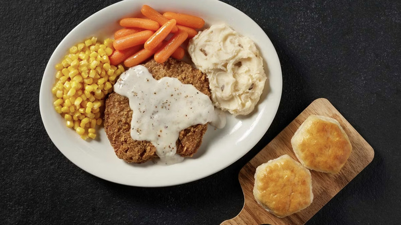 A chicken fried steak served with carrots, corn, mashed potatoes, and biscuits