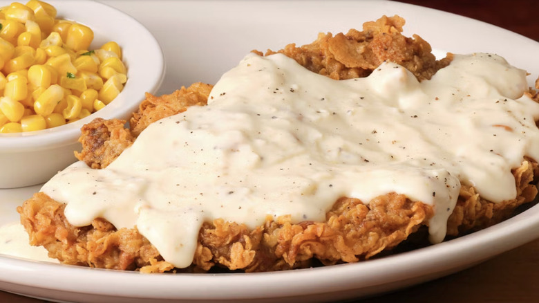 A chicken fried steak topped with white gravy and served alongside corn