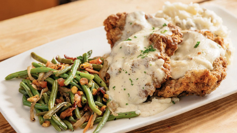 A large portion of chicken fried steak with roasted green beans and mashed potatoes