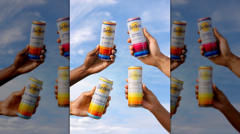 Hands holding Surfside cans against blue sky background