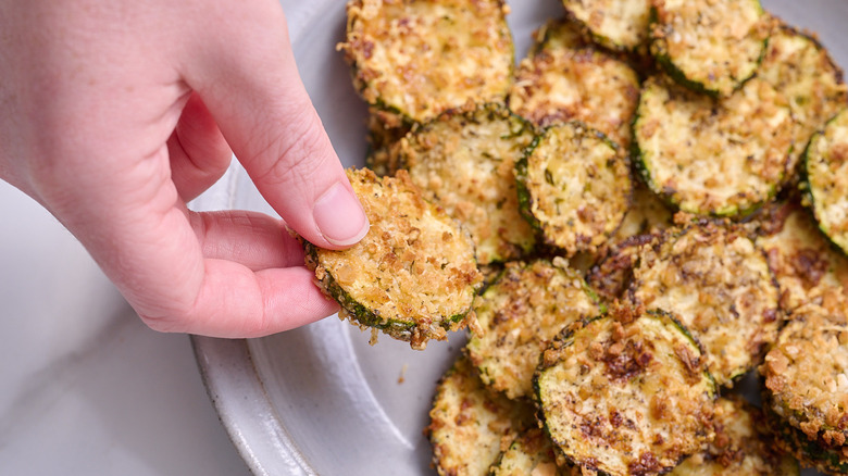 hand picking up a zucchini chip from bowl