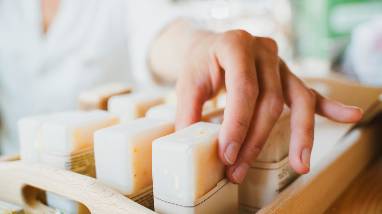 Close-up of person selecting bar soap from wooden tray