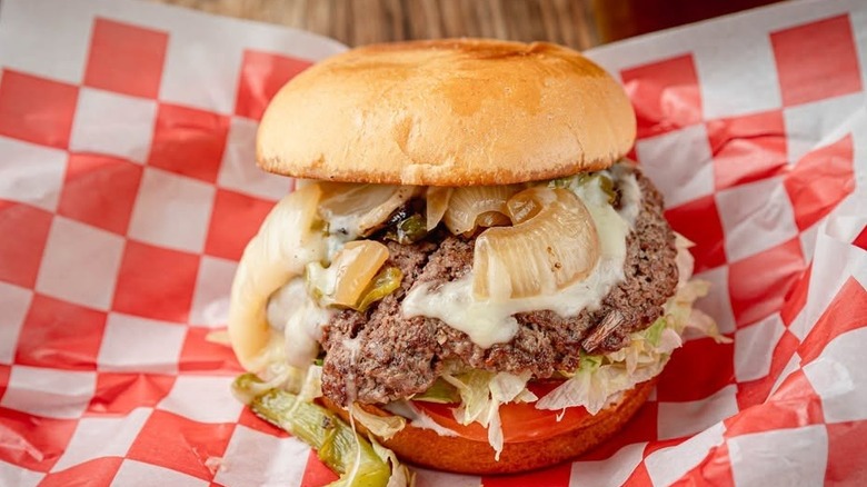 A beef burger with lettuce and onions on red and white paper