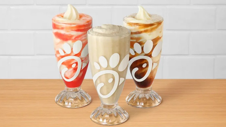 Three different flavors of Chick-fil-A Frosted Sodas on a wooden table with a white background