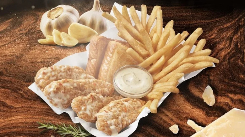 A Dairy Queen parmesan chicken strip basket with Texas toast and fries on a wooden table with pieces of garlic and parmesan next to it.
