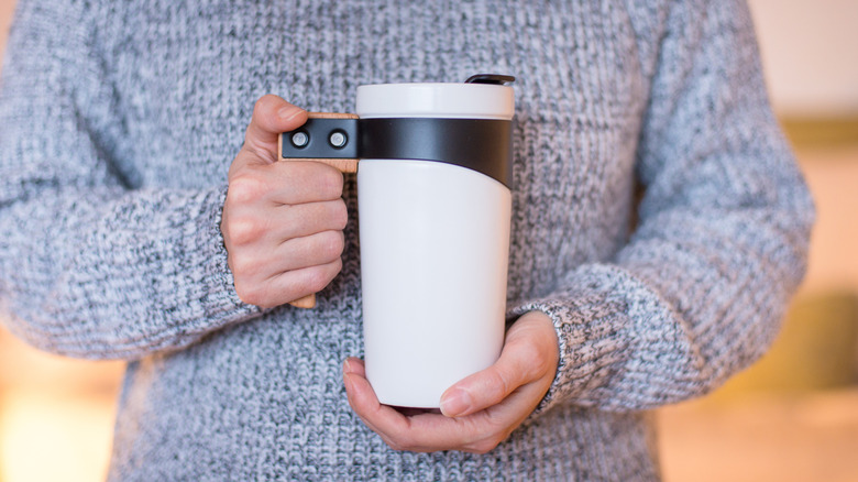 Person wearing a gray sweater holding a white travel mug
