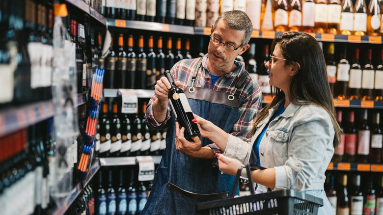 store owner showing wine bottle to woman