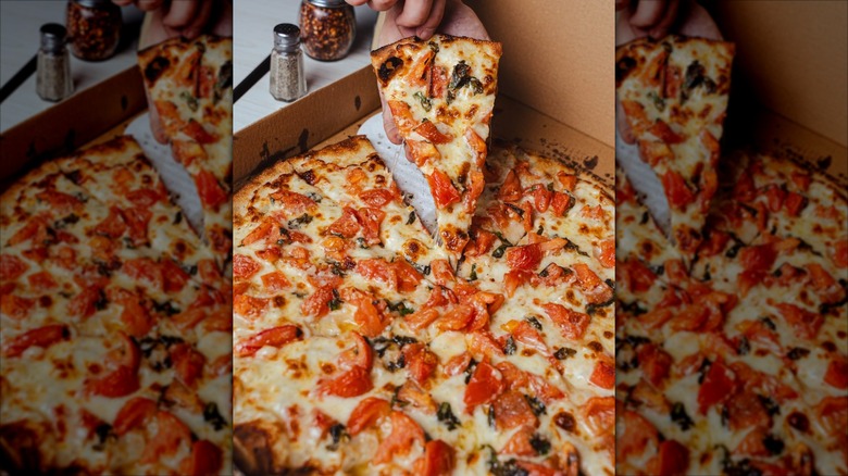 Hand picking up a slice of apizza from a whole pie in box