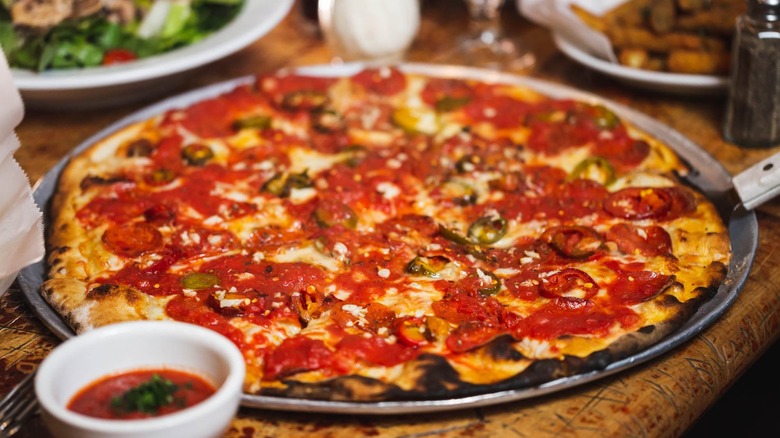 Thin crust pizza with pepperoni and peppers on silver tray with blurred salad