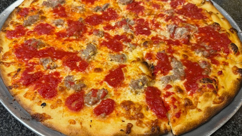 Round pizza with sausage on silver tray