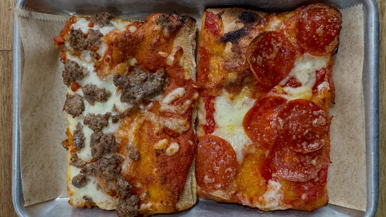 Slices of pepperoni and sausage pizza on paper in silver tray