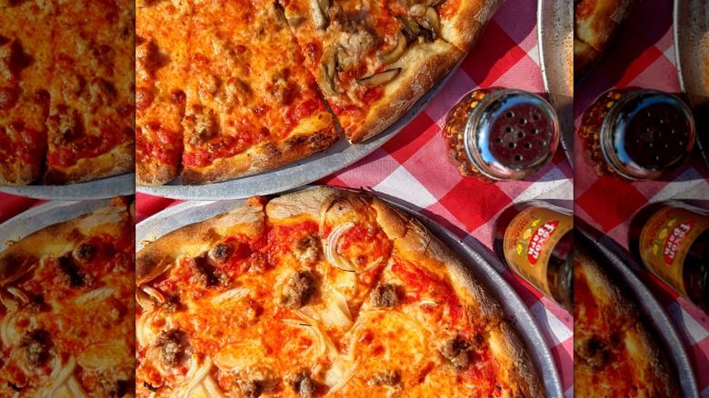 Two pizzas on red and white checked cloth with soda bottle and red pepper flakes