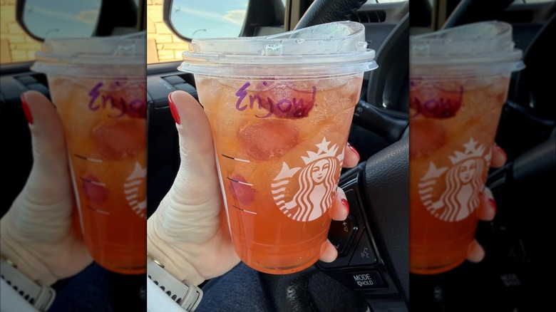 woman holding Starbucks Mango Strawberry Refresher in car