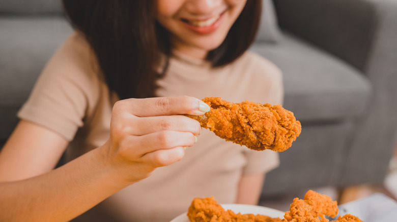 Smiling person holding piece of crispy fried chicken