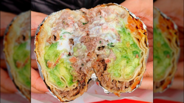 Hands holding burrito with sour cream, avocado and meat