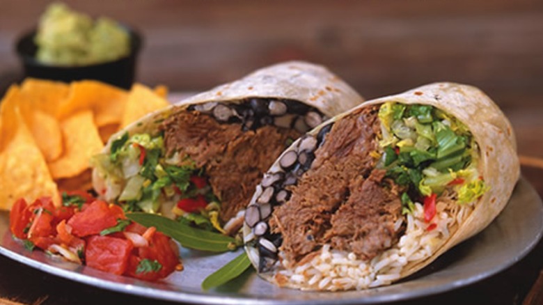 Steak burritos on a plate with chips and guac