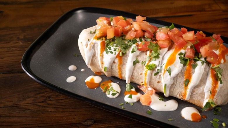 Burrito on black plate topped with crema, tomatoes, and cilantro