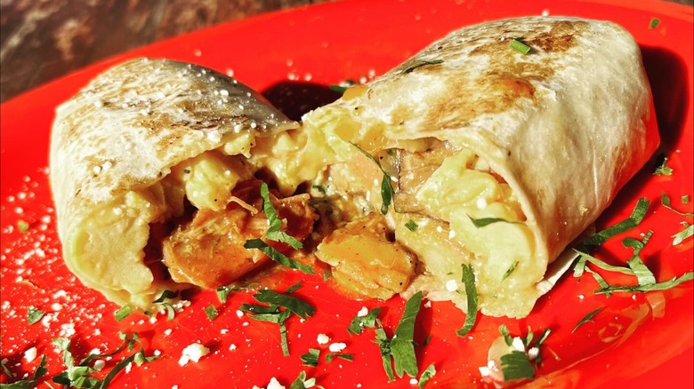 Red plate with breakfast burrito with potatoes