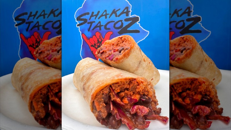 Burritos on white plate in front of Shaka Tacoz sign