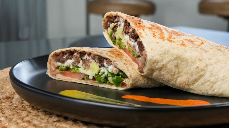 Burrito with steak and peppers on black plate