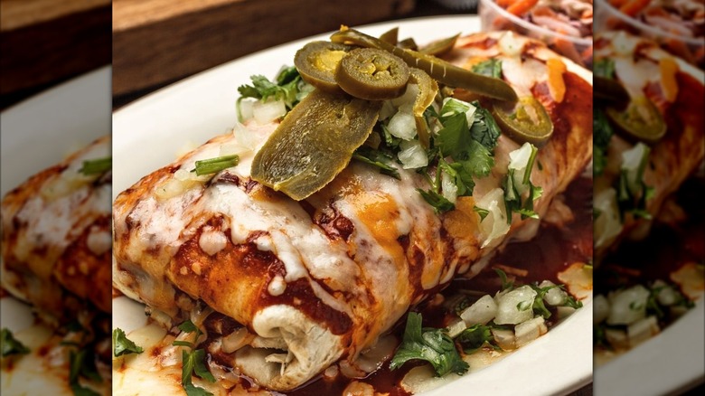 Burrito on white plate covered with cheese, sauce, and jalapenos