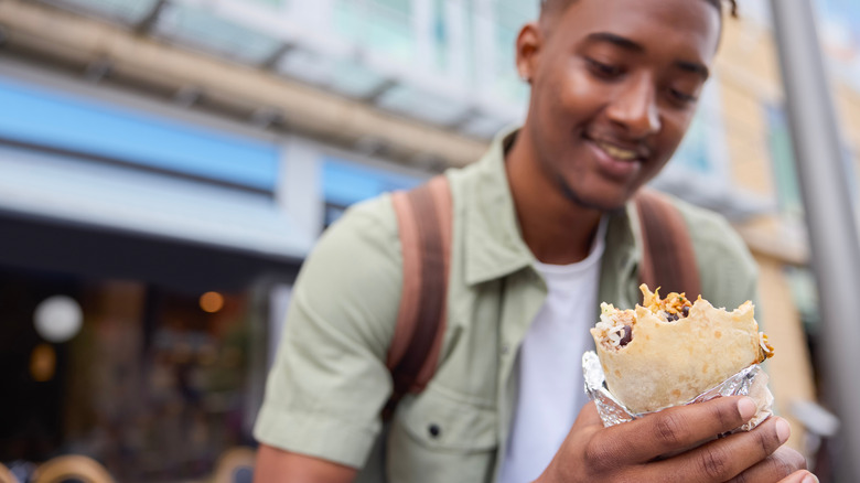 Man outside holding a burrito and smiling