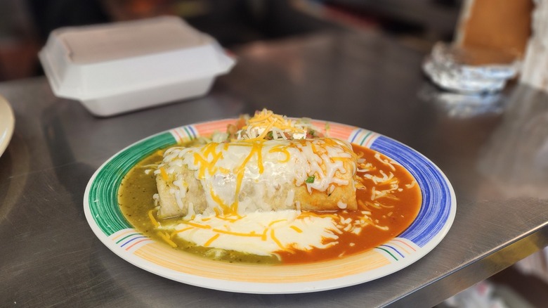 Wet burrito with red and green sauce and queso on plate