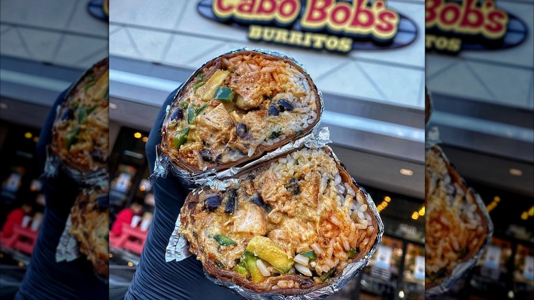 Holding two halves of a burrito in front of Cabo Bob's storefront