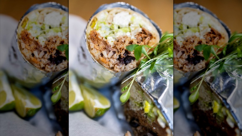 Two halves of a burrito with limes and greens