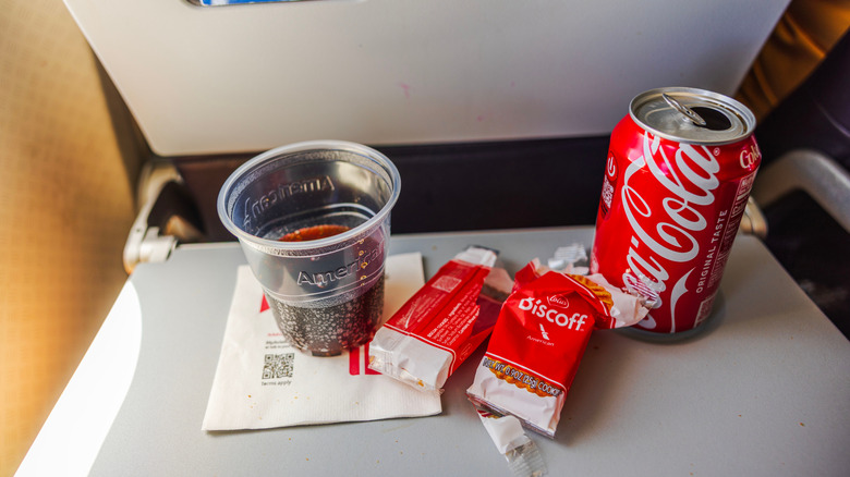Airplane tray table holding Biscoff cookies and can and cup of Coca-Cola