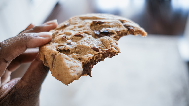 A hand holding a large chunk of a chocolate chip cookie