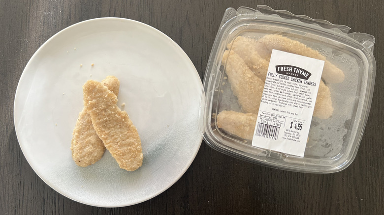 Plastic container of Fresh Thyme Market chicken tenders next to two tenders on white plate