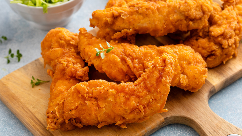 Battered chicken tenders piled onto wooden board with green herb garnish