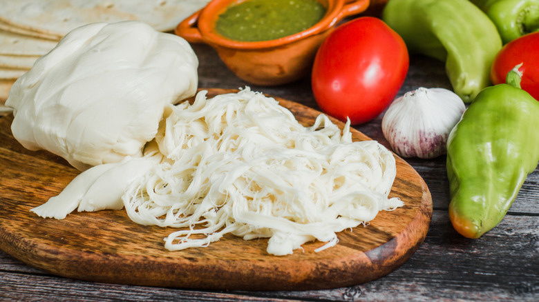 Oaxaca cheese on a wooden board with vegetables behind