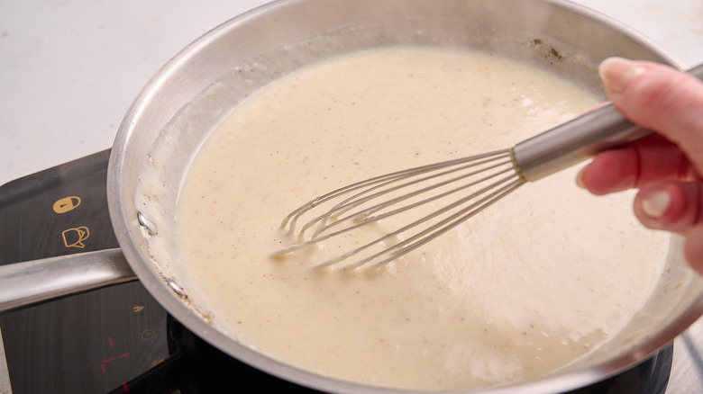 whisking cream sauce in a skillet