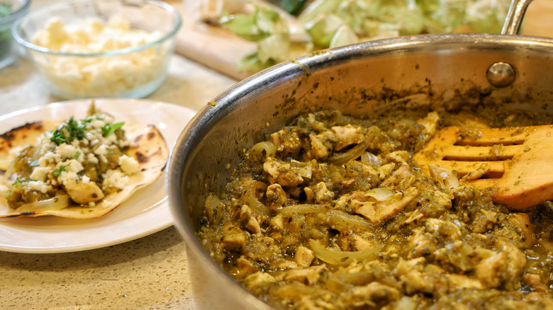 a verde chicken taco on a small plate next to a pan of chopped chicken and onions in salsa verde