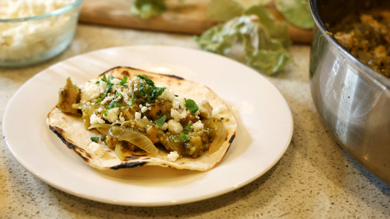 a charred corn tortilla topped with verde chicken, onions, queso fresco, and cilantro