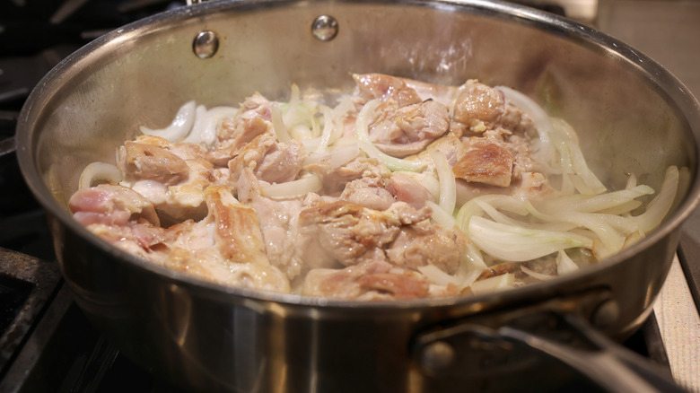 seared chicken thighs and sliced onions in a stainless steel pan