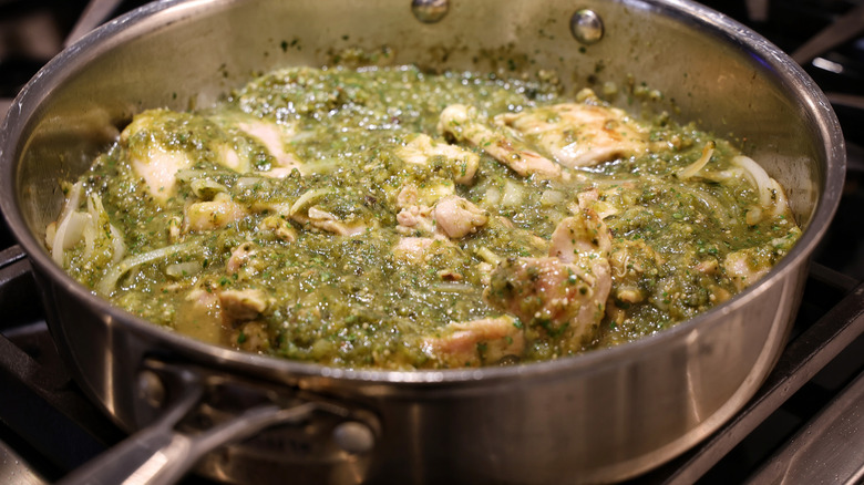 chicken thighs simmering in salsa verde in a stainless steel pan