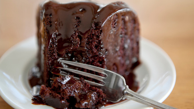 A fork piercing through a slice of decadent chocolate cake covered in melting fudge