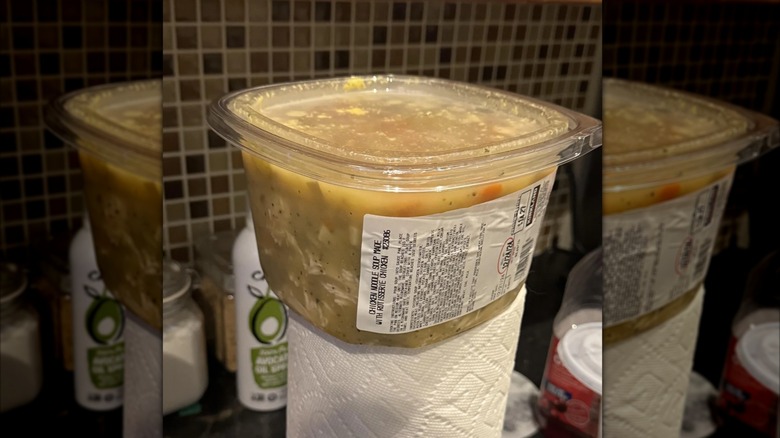 Plastic container of Costco chicken noodle soup rests atop a paper towel roll